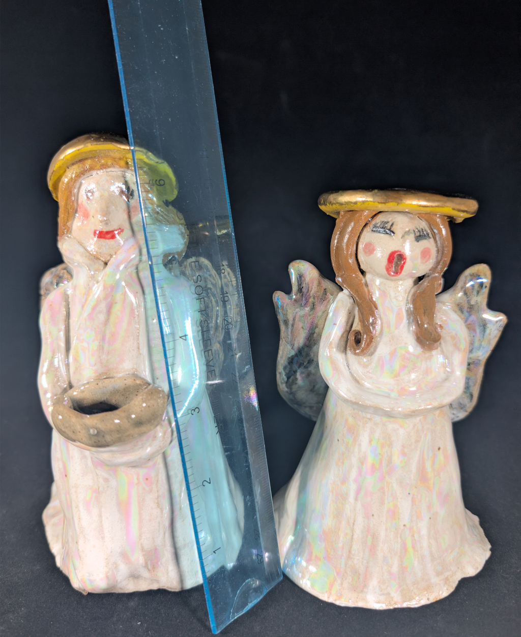 Two angel figurines, one in packaging, on a dark surface.