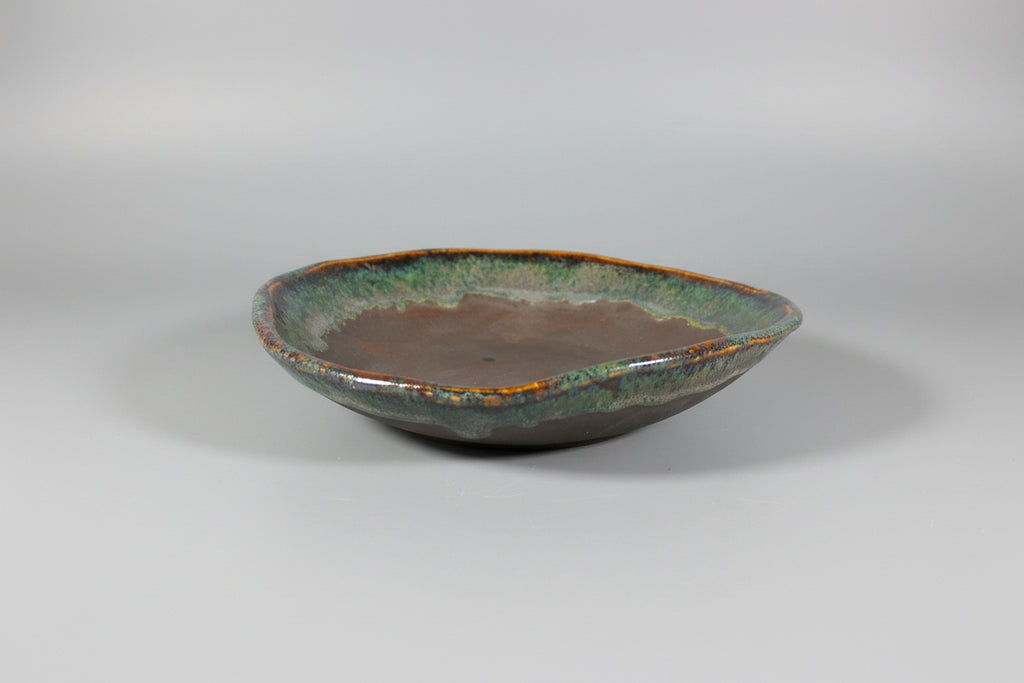 Ceramic dish with green and brown glaze on a black surface