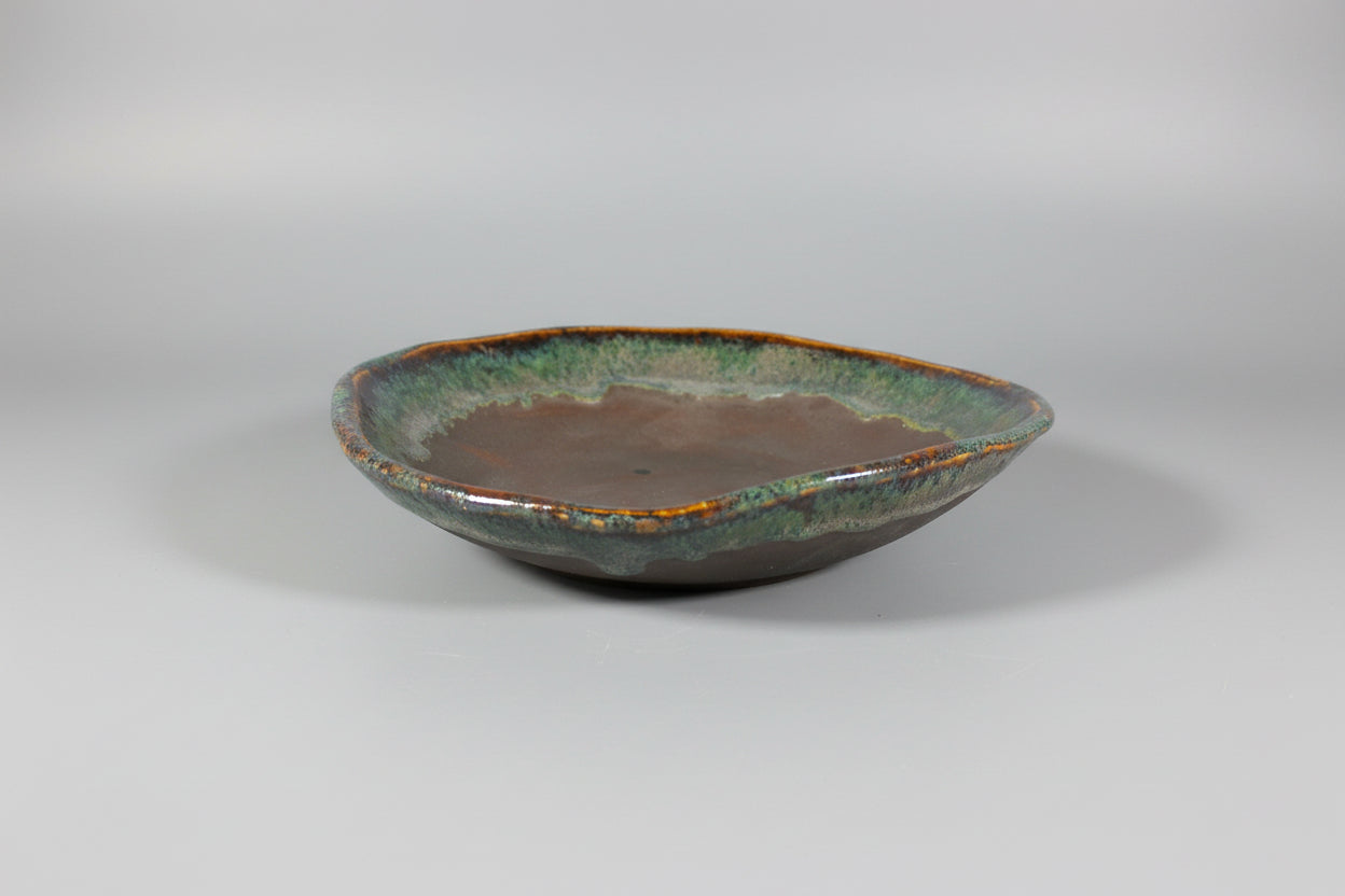 Ceramic dish with green and brown glaze on a black surface