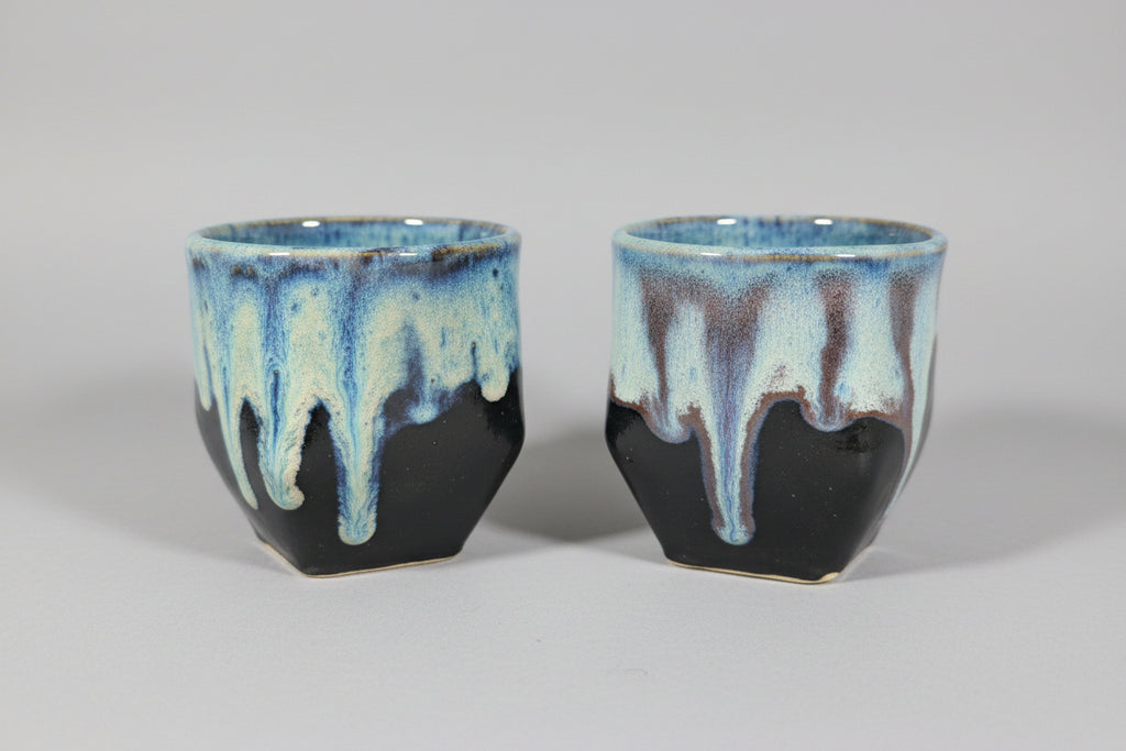 Two ceramic cups with blue and black glaze on a dark surface