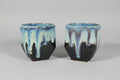 Two ceramic cups with blue and black glaze on a dark surface