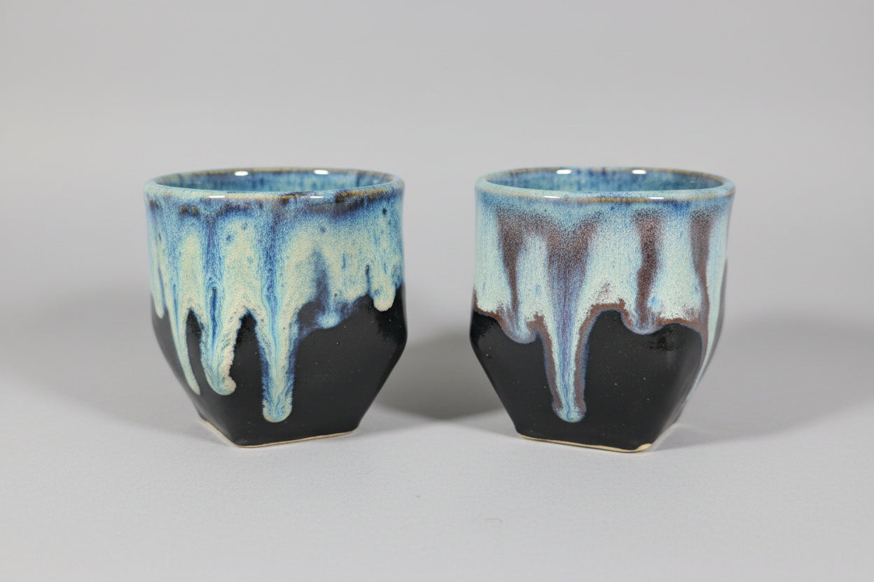 Two ceramic cups with blue and black glaze on a dark surface
