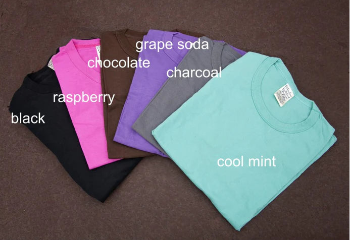 Folded t-shirts in various colors with labels on a brown background