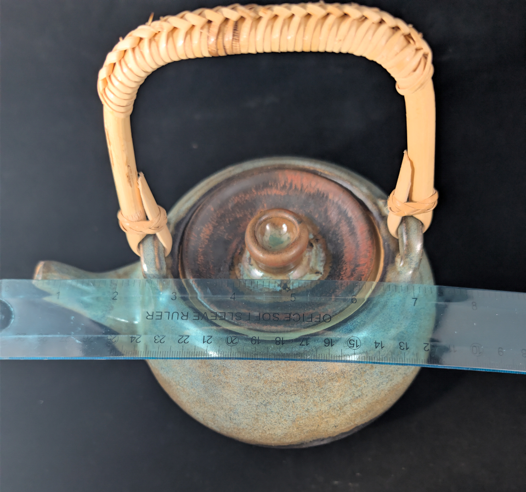 Ceramic teapot with wicker handle on a black background