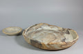 Two hand-carved stone plate and dipping dish with natural marbled patterns in beige, brown, and gray, displayed on a neutral gray studio background.