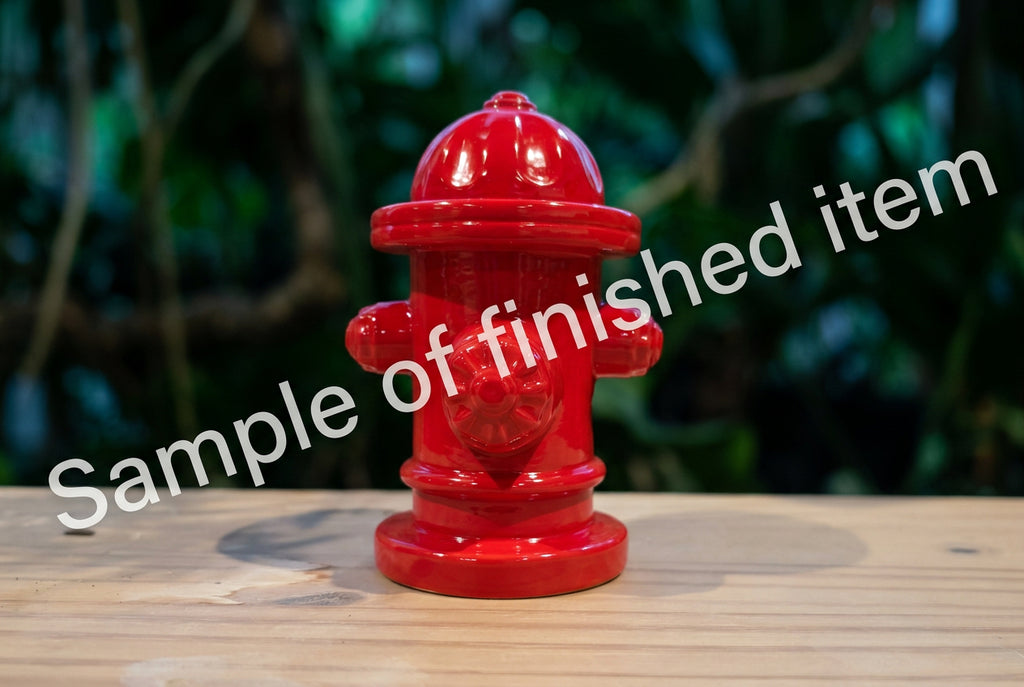 A small glossy red fire hydrant figurine standing on a light wood surface with a blurred gray background.